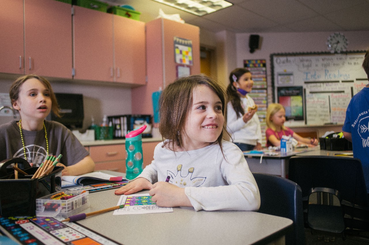 An AEES student smiles at her desk during classroom instruction.